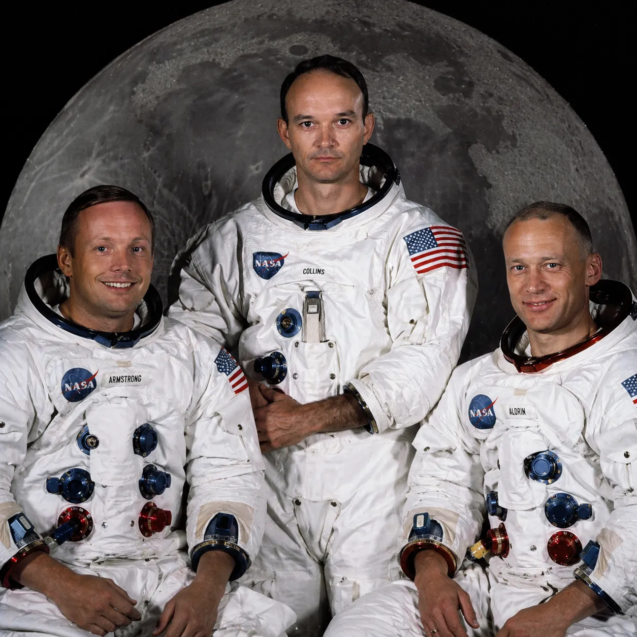 Apollo 11 crew — Armstrong, Collins, Aldrin — in front of a Moon backdrop